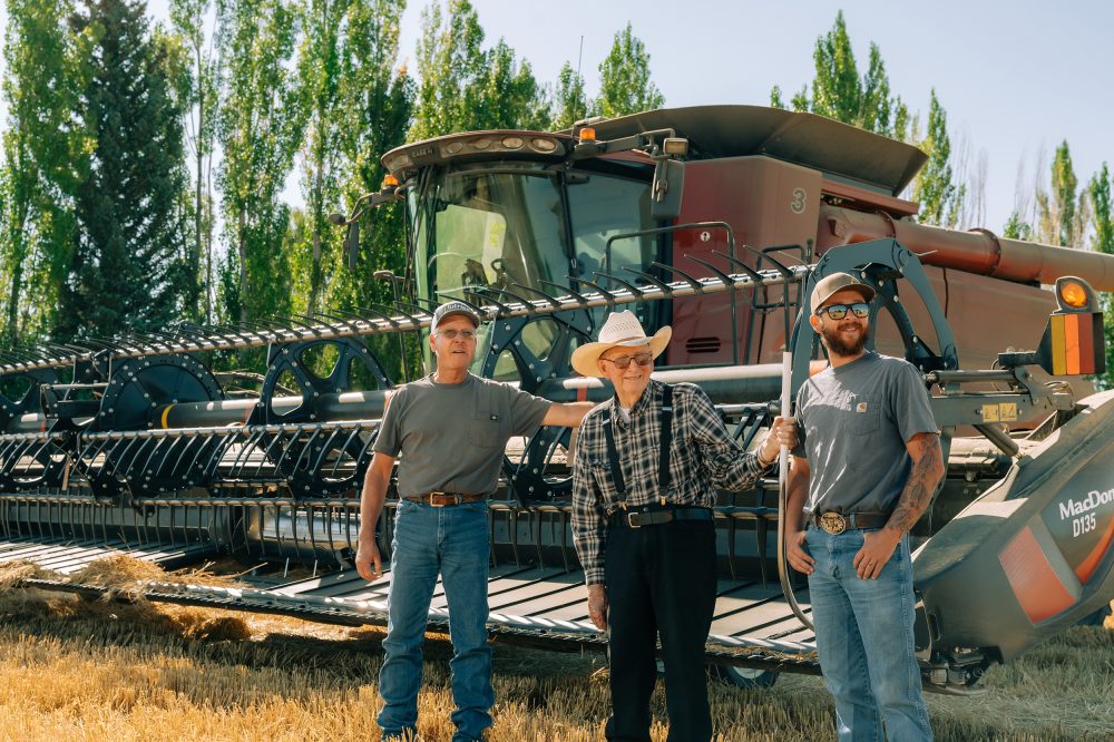Three men standing in front of a huge barley harvesting machine.