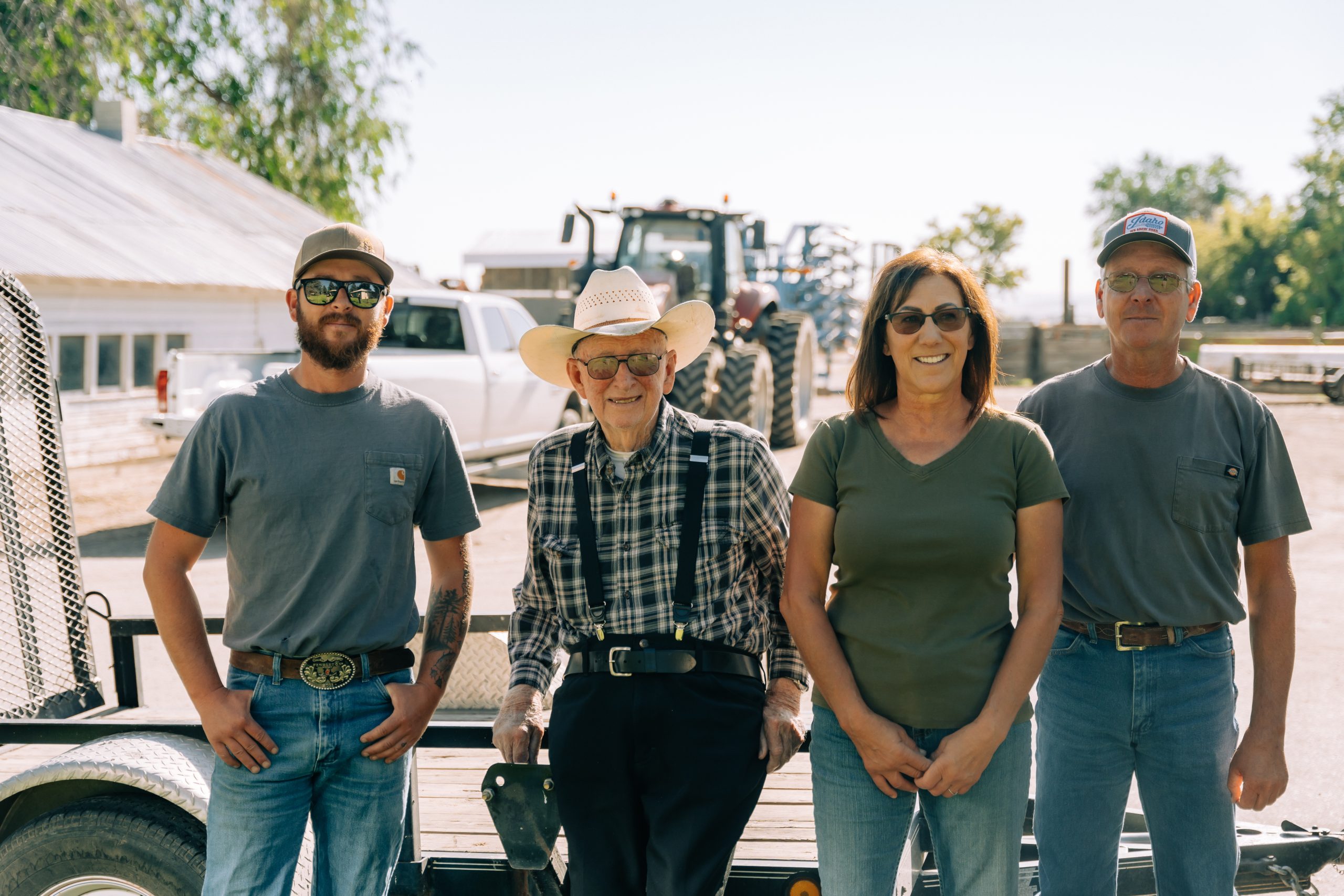 Three men and a woman leaning against a bed trailer with a tractor in the background.