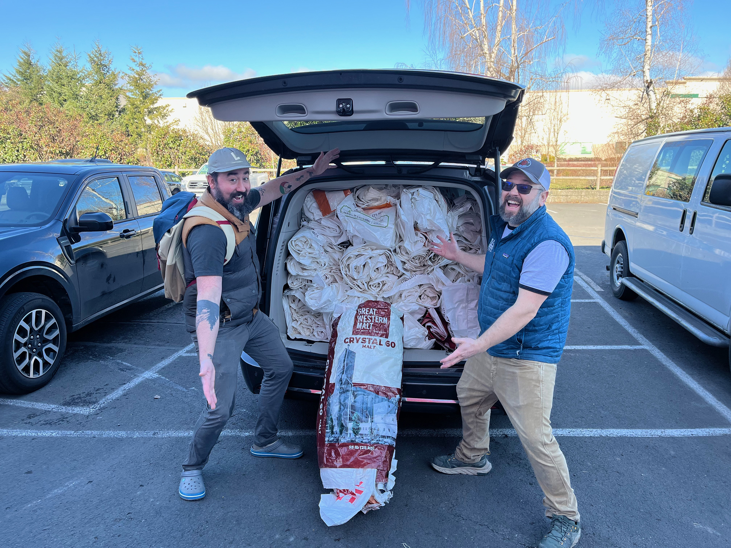 Sustainable-Brewing-malt-bag-recycling-sustainability Two men standing on either side of an open car trunk. The trunk is completely filled with empty malt bags.