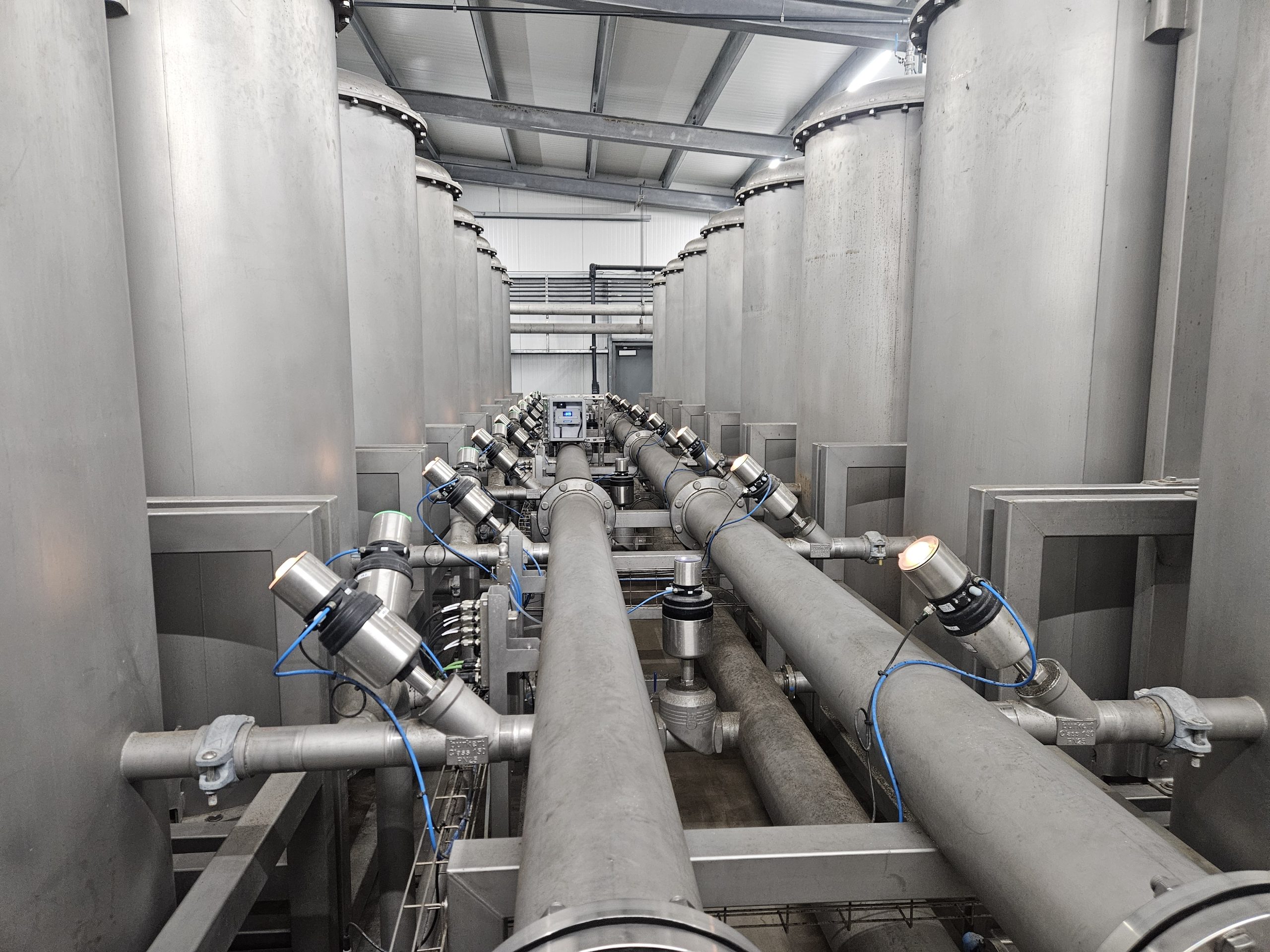 Sustainable Brewing Optisteep machine with a view of the pipes running between rows of large metal vats.